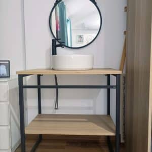 Mueble de baño moderno con estructura metálica negra y estantes de madera clara. Incluye lavabo blanco redondo en la parte superior y espejo circular con marco negro colgado encima.