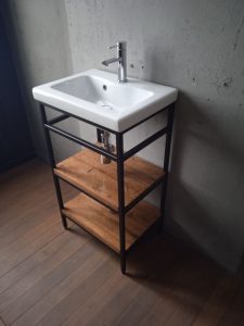 Lavabo moderno con estructura metálica negra, lavabo blanco rectangular y dos estantes de madera rústica, ideal para baños de estilo minimalista e industrial.