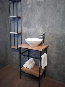 Lavabo de baño estilo industrial con estructura de metal negro y superficies de madera. Incluye una repisa inferior para almacenamiento y un toallero lateral. Elegante y funcional.