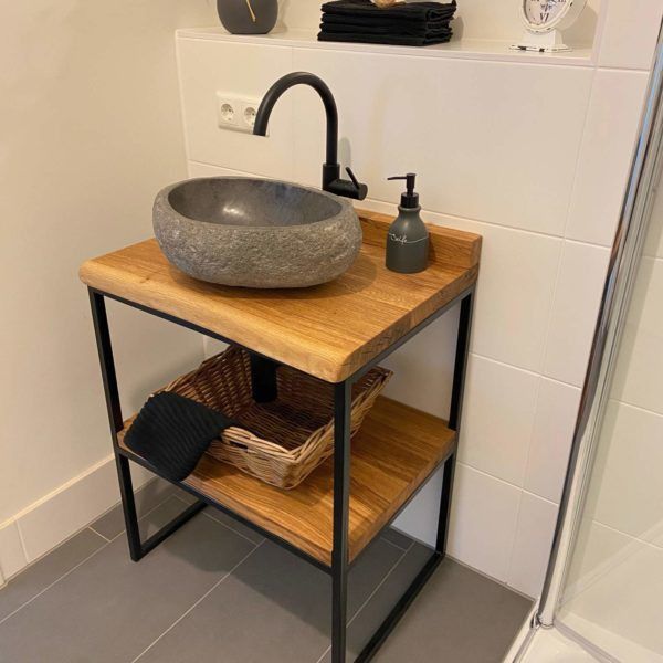 Lavabo moderno con encimera de madera, estructura de metal negro, lavabo de piedra gris y repisa inferior con cesta de mimbre. Diseño minimalista de baño compacto.