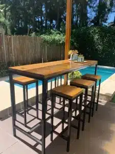 Conjunto de mueble de madera y metal con mesa alta rectangular y taburetes cuadrangulares, perfecto para exteriores. Ideal para reuniones junto a la piscina o en el jardín.