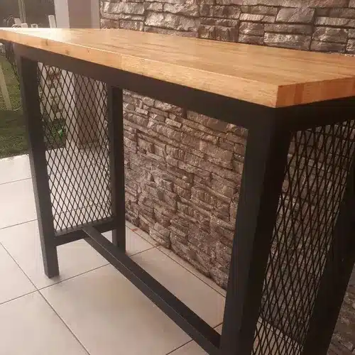 Mesa alta con tablero de madera clara y estructura metálica negra con diseño de rejilla. Ideal para ambientes industriales o modernos.