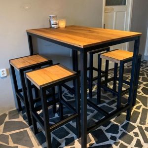 Mesa alta de comedor con diseño industrial, estructura metálica negra y tablero de madera. Incluye cuatro taburetes a juego, ideal para espacios pequeños y modernos.
