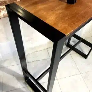 Mesa alta con diseño industrial, combinando una superficie de madera oscura y estructura metálica negra en forma de rectángulo, ideal para interior contemporáneo.