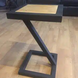 Mesa auxiliar moderna con estructura negra en forma de Z y tablero cuadrado de madera clara. Perfecta para decorar salones o salas de estar con estilo contemporáneo.