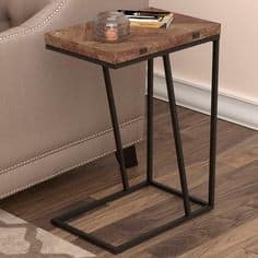 Mesa auxiliar con estructura de metal negro y tablero de madera rústica. Diseño moderno en forma de C, ideal para espacios pequeños junto a un sofá.