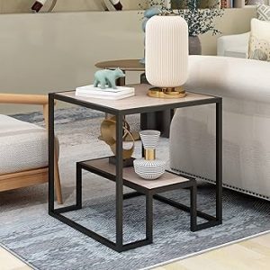 Mesa auxiliar de madera clara con estructura de metal negro en forma cúbica, decorada con objetos escultóricos y lámpara blanca, situada entre sofás en una sala contemporánea.