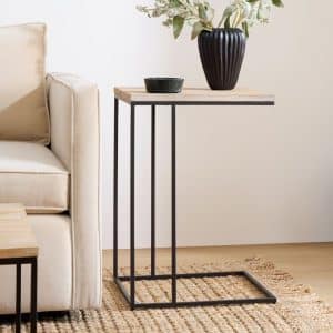 Mesa auxiliar moderna con estructura de metal negro y tapa de madera clara, junto a un sofá beige. Ideal para espacios minimalistas.