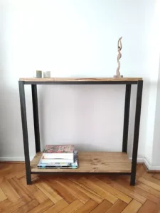 Mesa auxiliar de estilo industrial con estructura de metal negro y dos estantes de madera. Superior con adorno, inferior con revistas. Diseño minimalista y funcional.