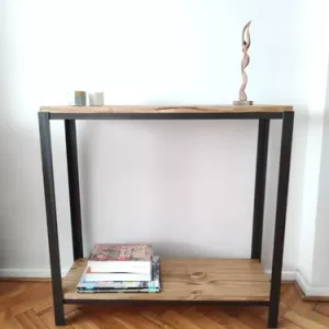 Mesa auxiliar de estilo industrial con estructura de metal negro y dos estantes de madera. Superior con adorno, inferior con revistas. Diseño minimalista y funcional.