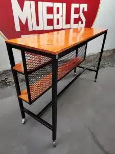 Mesa alta de estilo industrial con estructura de metal negro, superficie y estantes de madera, y ruedas para fácil movilidad. Ideal para cocina o bar.