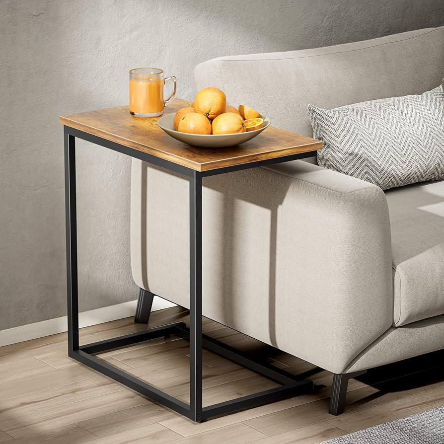 Mesa auxiliar moderna con estructura metálica negra y superficie de madera. Ideal para espacios compactos, colocada junto a un sofá beige, perfecta para bebidas y decoración.