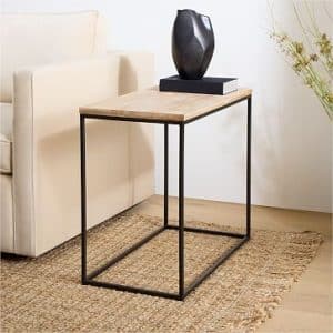 Mesa auxiliar moderna con estructura de metal negro y superficie de madera clara. Ideal para espacios contemporáneos. Se encuentra sobre una alfombra tejida de color neutro.