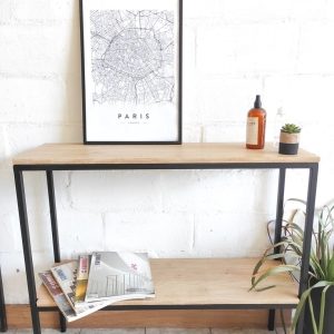 Mesa consola de dos niveles con estructura de metal negro y superficies de madera clara. Ideal para decoración minimalista en salas o recibidores.