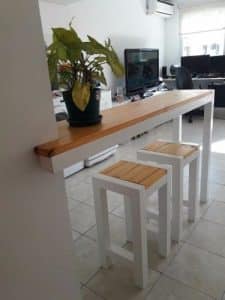 Barra de madera con patas blancas, acompañada de dos taburetes a juego. Ideal para espacios de cocina o comedor, ofrece un diseño moderno y funcional.