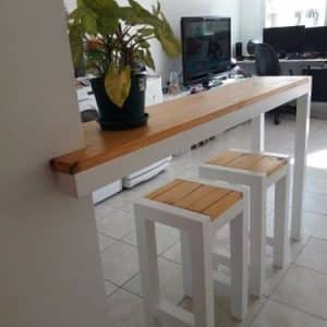 Barra de madera con patas blancas, acompañada de dos taburetes a juego. Ideal para espacios de cocina o comedor, ofrece un diseño moderno y funcional.