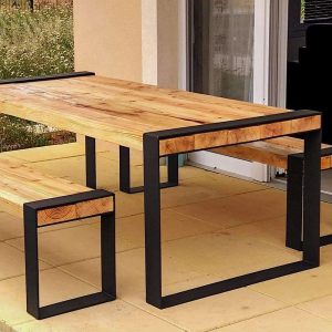 Mesa de madera con estructura metálica negra minimalista. Tiene un acabado natural y está acompañada por un banco a juego, ideal para exteriores.