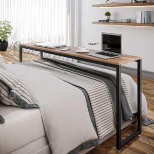 Mesa de trabajo estrecha y alargada con tablero de madera y base de metal negro, colocada detrás de una cama en habitación moderna.