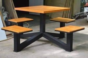 Mesa cuadrada de madera con base metálica negra y cuatro asientos integrados del mismo material y diseño. Ideal para exteriores o áreas de descanso. Diseño moderno y funcional.