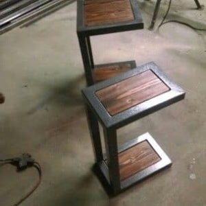 Mesa decorativa en forma de zigzag, con estructura metálica oscura y superficies de madera pulida. Ideal para espacios modernos o industriales.