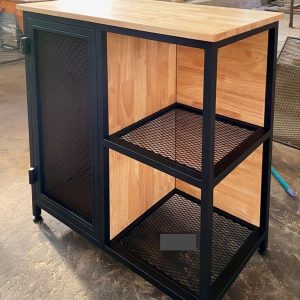 Mueble industrial con estructura de metal negro y superficies de madera clara. Incluye una puerta con rejilla y estantes de malla metálica. Ideal para almacenamiento.