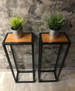 Dos modernos pedestales de metal negro con superficie de madera, ideales para plantas o decoraciones. Diseño minimalista, estructura alta y abierta, perfecta para interiores contemporáneos.