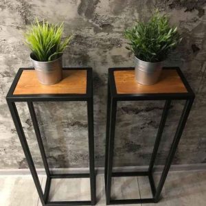 Dos modernos pedestales de metal negro con superficie de madera, ideales para plantas o decoraciones. Diseño minimalista, estructura alta y abierta, perfecta para interiores contemporáneos.