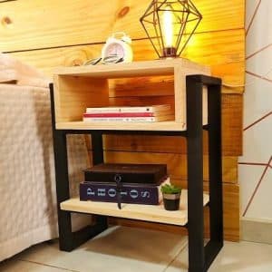 Mesa de noche de madera y metal con dos estantes. Incluye decoración con libros, cajas y una lámpara geométrica. Diseño moderno y funcional para dormitorios.