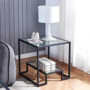 Mesa auxiliar moderna con estructura de metal negro y tablero de vidrio transparente, incluye un estante inferior. Ideal para decorar un salón o sala de estar contemporánea.