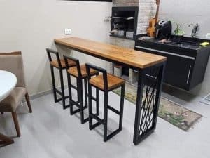 Barra alta de madera con estructura metálica negra, acompañada de tres taburetes a juego. Diseño moderno y elegante, ideal para cocina o bar en el hogar.