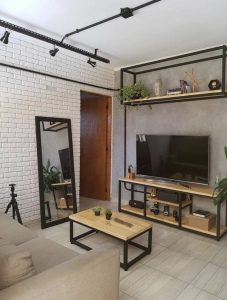 Centro de entretenimiento moderno con estructura de metal negro y estantes de madera. Incluye soporte para TV, espacio para libros, plantas y decoración. Estilo industrial minimalista.