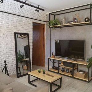 Centro de entretenimiento moderno con estructura de metal negro y estantes de madera. Incluye soporte para TV, espacio para libros, plantas y decoración. Estilo industrial minimalista.