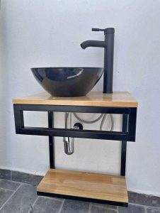 Lavabo moderno con encimera de madera clara, estructura metálica negra, lavamanos redondo negro y grifo a juego. Diseño minimalista y funcional, ideal para baños contemporáneos.