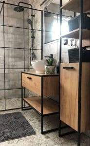 Mueble de baño estilo industrial con estructura de metal negro y superficies de madera clara. Incluye lavabo blanco, estantes abiertos y cajones, ideal para almacenamiento funcional y moderno.