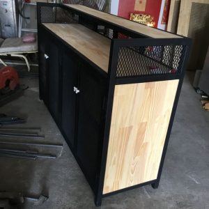 Mueble de almacenamiento rectangular con estructura de metal negro y paneles de madera clara. Tiene puertas de malla metálica y superficie lisa, ideal para espacios industriales o rústicos.