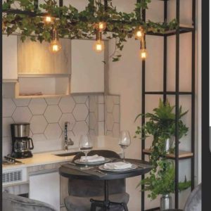 Mesa alta redonda con sillas acolchadas de terciopelo gris, conjunto ideal para un comedor moderno. Estructura metálica negra con estantería y plantas decorativas.