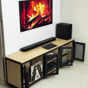 Mueble de TV moderno con superficie de madera clara y puertas de malla metálica negra. Incluye varios compartimentos para almacenamiento y ruedas para fácil movilidad.
