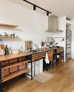 Cocina minimalista con estanterías abiertas de madera clara y metal negro, encimera integrada con fregadero y cestas de almacenamiento tejidas. Diseño funcional y organizado.