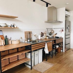 Cocina minimalista con estanterías abiertas de madera clara y metal negro, encimera integrada con fregadero y cestas de almacenamiento tejidas. Diseño funcional y organizado.