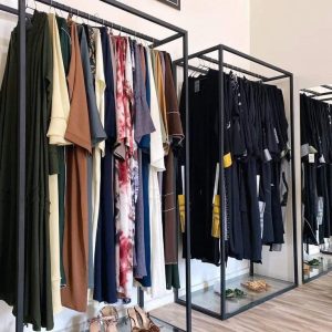 Mueble de metal negro estilo percha con base de vidrio, ideal para exhibir ropa y zapatos en una boutique moderna.