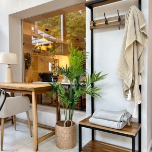 Banco de almacenamiento de madera con estructura metálica negra, incluye perchero con ganchos superiores para colgar abrigos. Diseño minimalista ideal para entradas o recibidores.