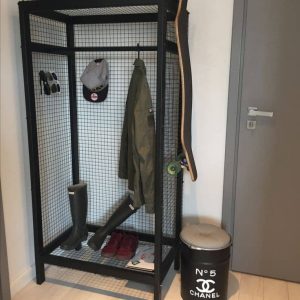 Estante de rejilla negra con acabados industriales, equipado con espacio para colgar ropa y almacenar objetos. Ideal para decoración moderna y almacenamiento en el hogar.