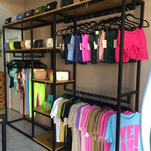 Estantería metálica negra con baldas de madera, ideal para organizar ropa y accesorios en una tienda. Incluye barras para colgar prendas y espacio superior para exhibir productos.