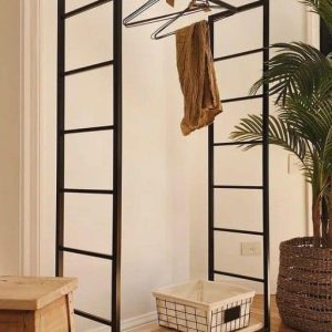 Perchero metálico negro con ruedas, barras laterales y estante inferior de madera. Incluye colgadores y una cesta blanca. Diseño minimalista para el hogar.