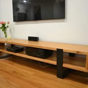 Mueble bajo de madera clara con diseño moderno, cuenta con estantes abiertos y patas de metal negro, ideal para colocar equipos electrónicos en una sala de estar.