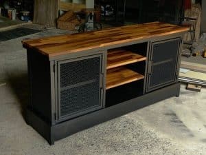 Mueble de estilo industrial con estructura negra y puertas de rejilla metálica, acompañado de una resistente tapa de madera y estantes abiertos al centro. Ideal para almacenaje.