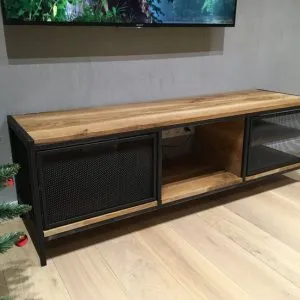 Mueble de TV estilo industrial con estructura de metal negro y superficie de madera. Cuenta con dos puertas de malla metálica y un espacio central abierto.