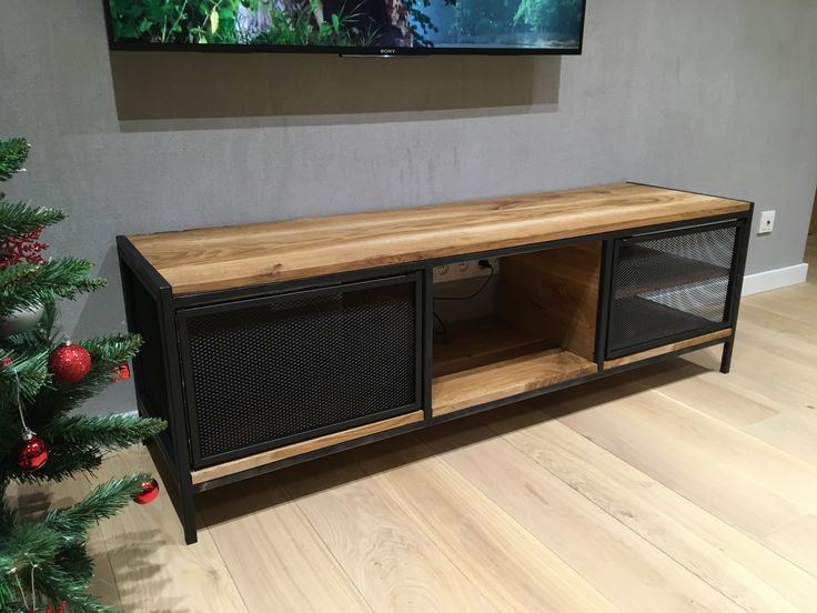 Mueble de TV estilo industrial con estructura de metal negro y superficie de madera. Cuenta con dos puertas de malla metálica y un espacio central abierto.