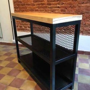 Estantería industrial de metal negro con dos estantes de malla y una superficie de madera clara, ubicada sobre un suelo de baldosas coloridas frente a una pared de ladrillo visto.