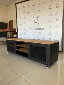 Mueble TV moderno de metal negro y madera, con estantes abiertos y puertas de rejilla, montado sobre ruedas para fácil movilidad. Ideal para sala de estar contemporánea.